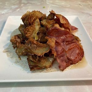 Plato de alcachofas fritas con jamón y salsa de hongos